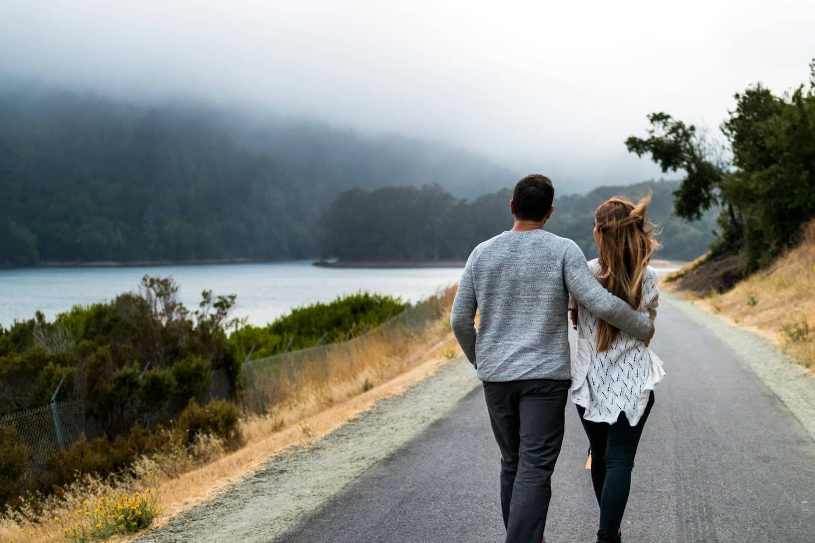 Un couple qui marche côte à côte sur une route au bord d’un lac