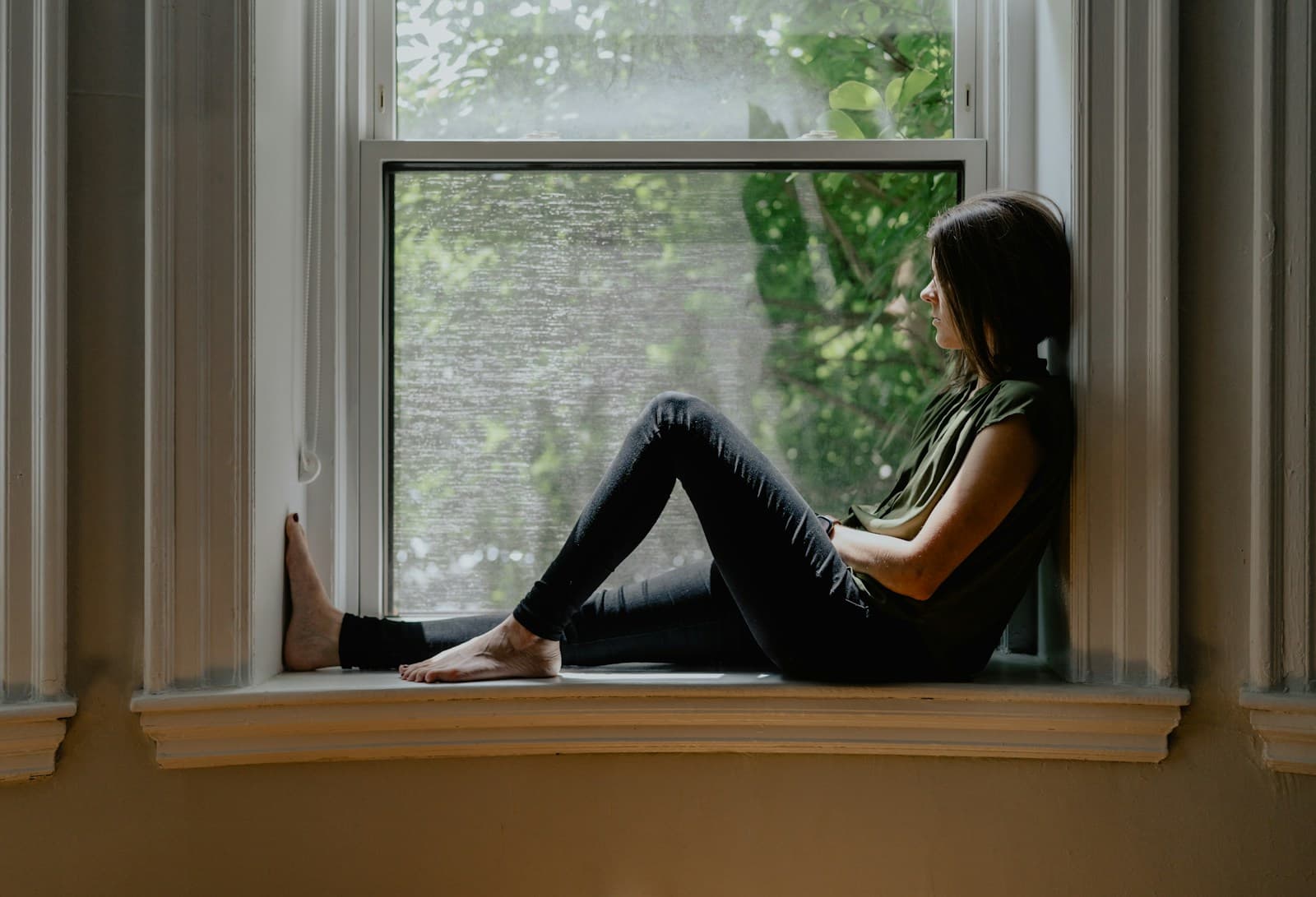 Une personne assise sur le rebord d’une fenêtre, le regard tourné vers l’extérieur